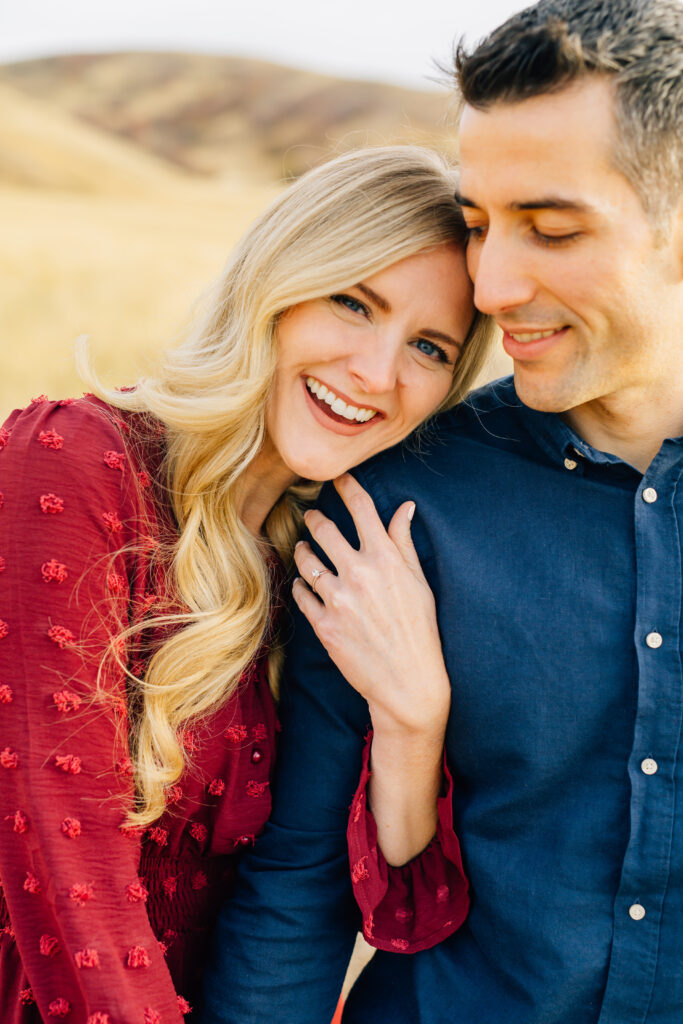 An image of a woman leaning on a man with her arm around his arm with yellow hills behind them.